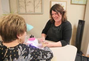 Woman smiling while she does another woman's nails
