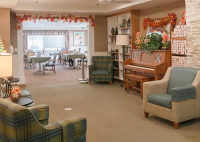 Living room with chairs and a piano overlooking a dining room